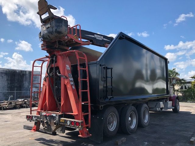 Peterbilt 388 grapple truck with a large dump body and hydraulic crane, side view showing rear grapple attachment and multiple axles.