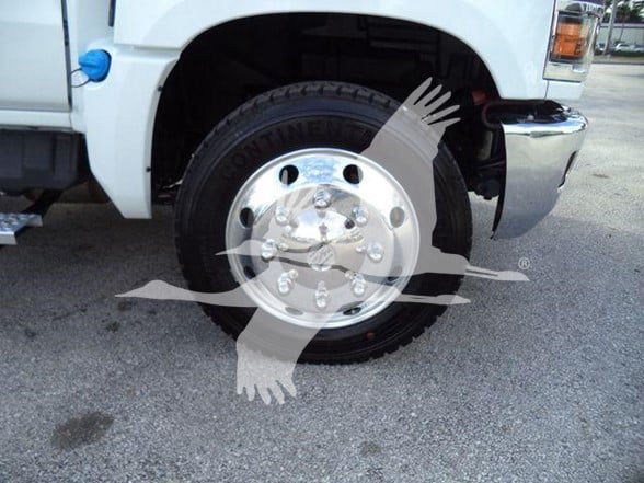 Chevrolet Silverado 6500HD front wheel area showing GM hubcap and Conti? tire with visible text, partial truck body and chrome bumper.