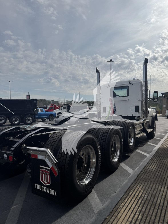 Kenworth T880 tractor in a parking lot, three rear axles, white sleeper cab, dual exhaust stacks, mud flaps with TruckWorx logo.