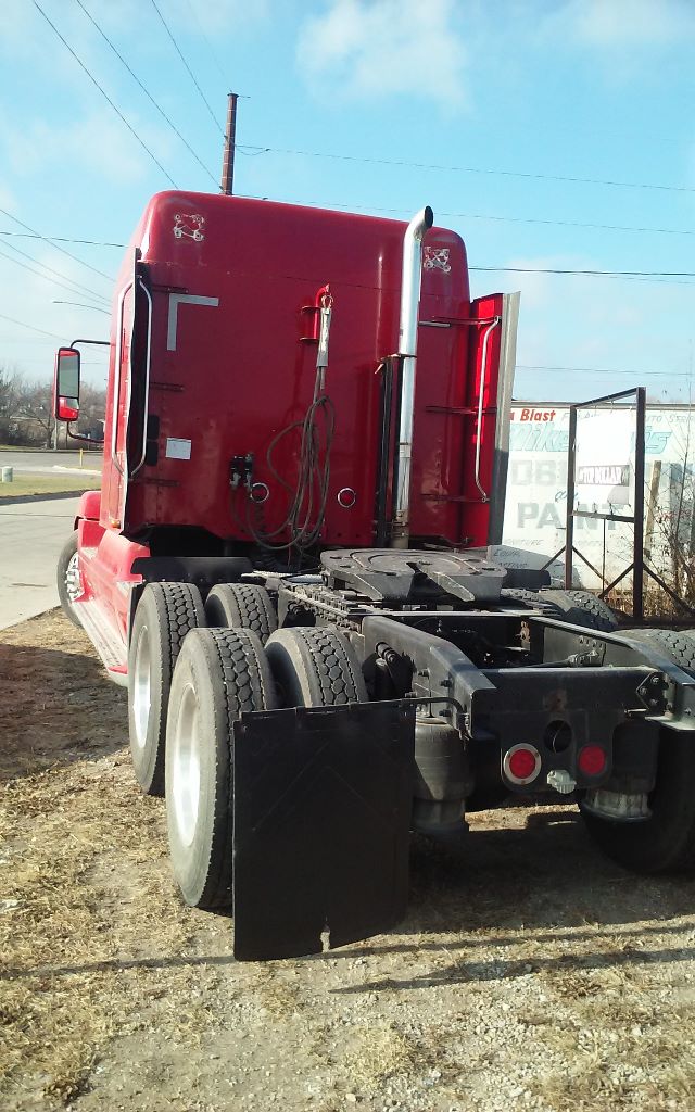 Truck back view showing red Freightliner conventional cab with dual rear axles and fifth wheel, black mud flaps, and rear lights.