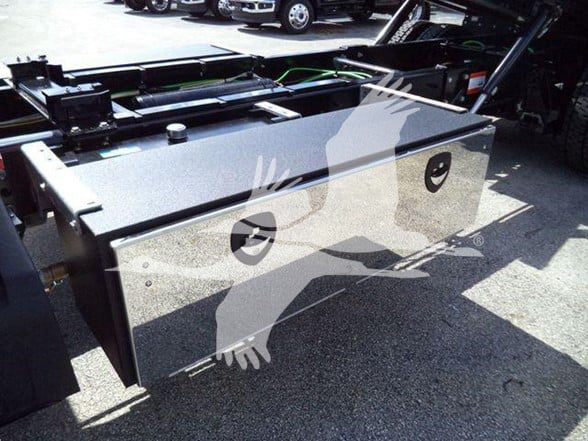 Flatbed truck storage box mounted on chassis with a glossy gray surface, two circular access ports and a handle, hydraulic components in background. watermark of a bird image overlay.