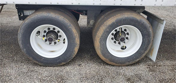 Trailer wheels and dual-axle setup of a 2024 Vanguard VXP dry van showing white rims and tires on gravel surface.