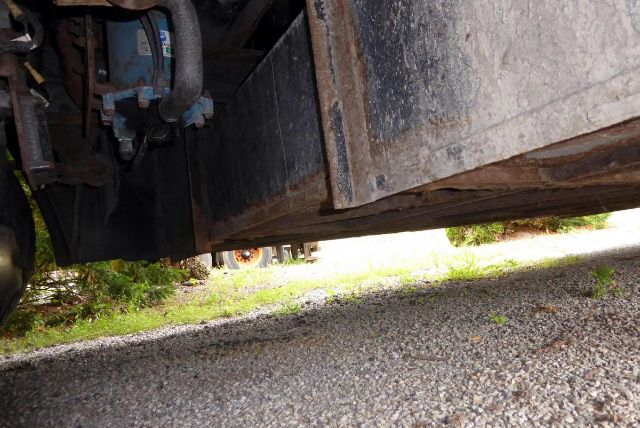 Underbody view of a Bluebird All American bus showing chassis, frame, and underside details with a gravel surface.