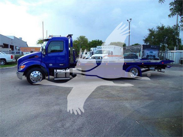 Blue Peterbilt 536 tow truck with extended flatbed, side view showing cab and long bed in a dealership lot.