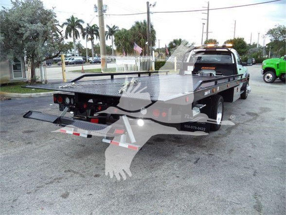 Ram 5500 tow truck flatbed rear view showing electrical hookups and taillights, with a black flatbed and wheel chocks; dealership watermark overlay across image.