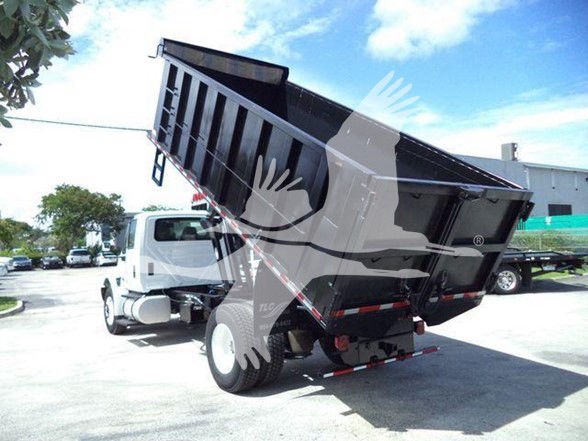 Dump truck in raised mid-dump position showing cargo bed and rear wheels with International badge and truck cab in background.