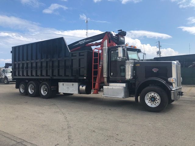 Peterbilt 388 dump truck with crane in side view showing large black dump body and chrome cab.