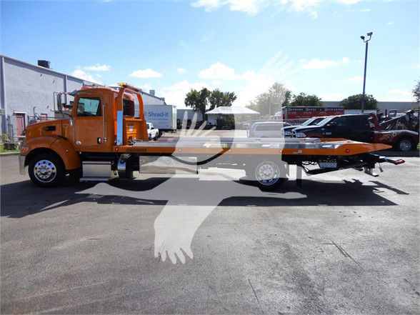 Side view of a bright orange 2022 Peterbilt 337 tow truck with a flatbed, long wheelbase, and chrome fuel tanks.