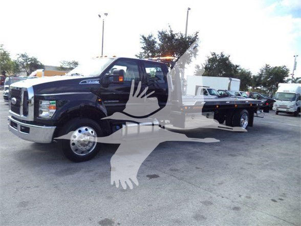 Ford F750 XLT tow truck in dark blue with flatbed, front chrome grille, large dual rearview mirrors.