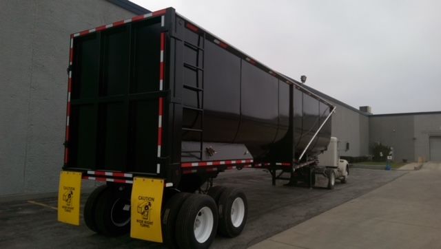 Great Dane 40 ft round bottom dump trailer viewed from rear-left with black body and yellow caution mud flaps.