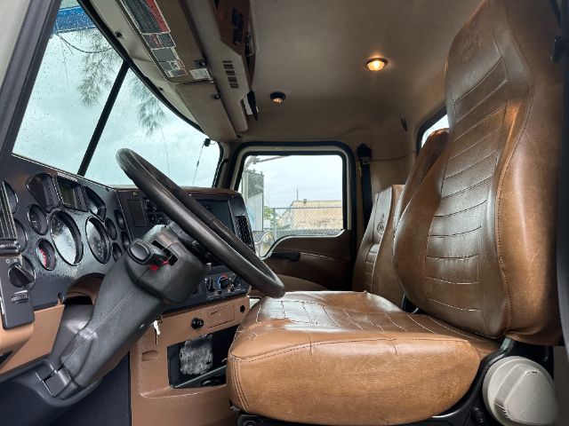 Cab interior of a 2017 Mack GU713 vacuum truck showing brown leather driver and passenger seats, steering wheel, dashboard, and window view.