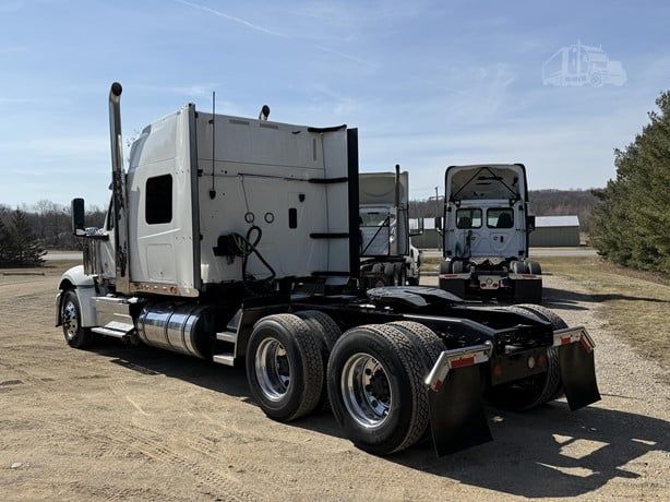 Truck tractor with sleeper cab, rear view showing dual rear axles and fifth wheel, exterior chrome fuel tanks, and back of cab.