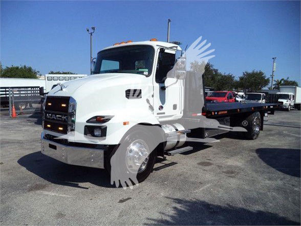 2024 Mack MD6 tow truck in white, side view showing front grille, hood, cab, and flatbed with wheel chocks and side mirrors.