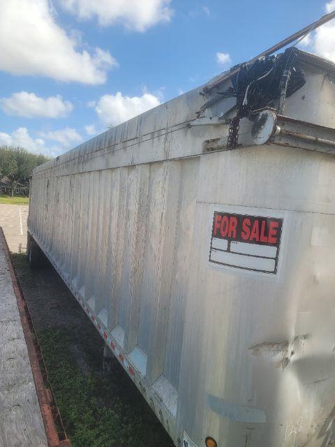 Trailer side with 'FOR SALE' sign and metal exterior; chain mechanism on top; blue sky with clouds.