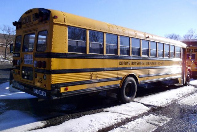 Yellow school bus with black stripes showing Kidzone Transportation Division text along side, rear and windows, bus number 22, snow on ground.
