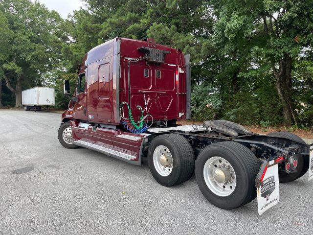 Freightliner Cascadia truck cab with maroon color, rear view showing twin rear axles and fifth wheel. Visible lines and hoses near cab, no legible serials or labels.