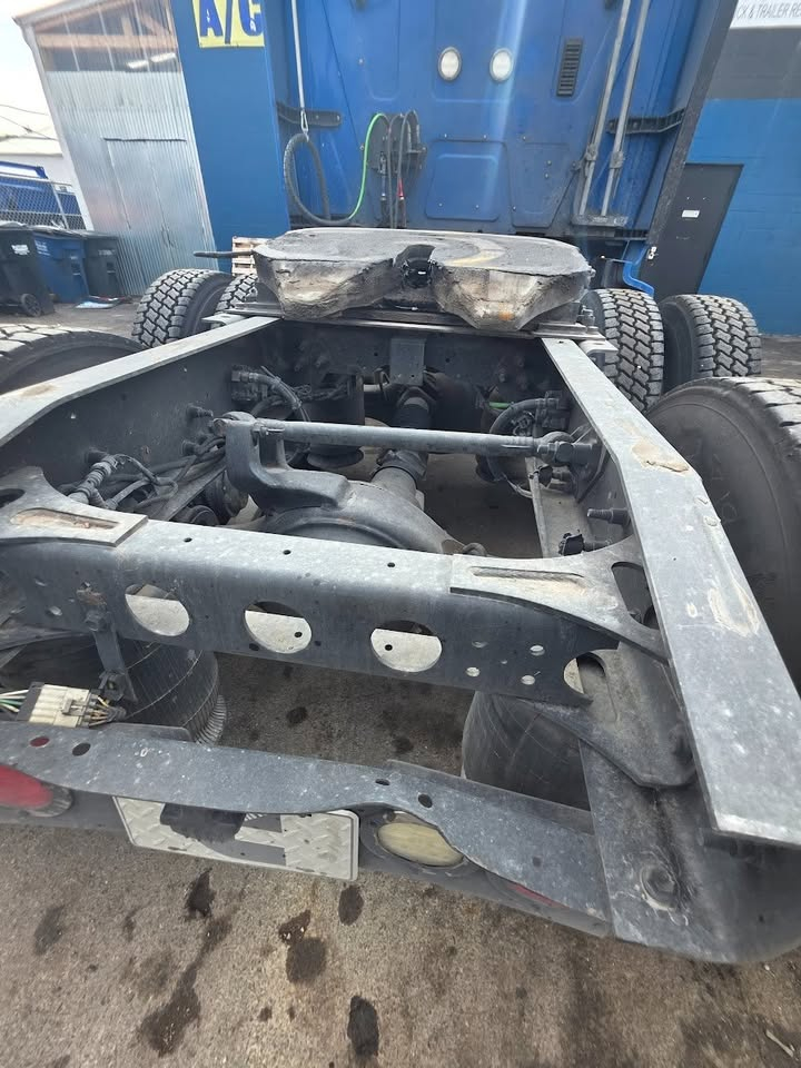 Truck chassis rear view showing ISX engine area, fifth wheel mount, frame rails, drive axle, suspension components and exposed wiring.