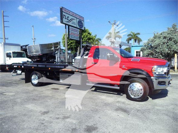 2024 Ram 5500 SLT tow truck with flatbed, red cab, chrome wheels, side view showing VIN and stock number and dealership lot.