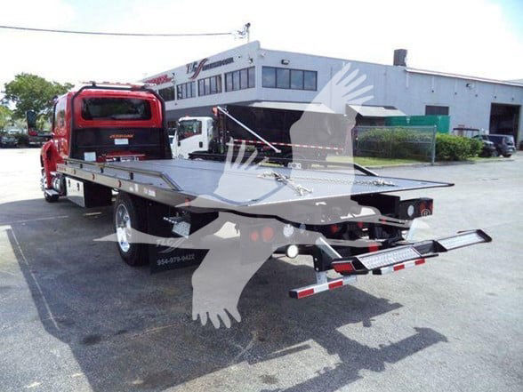 Tow truck with a flatbed in a dealership lot, International MV model, stock number J24054FM; rear view showing platform and ramp.