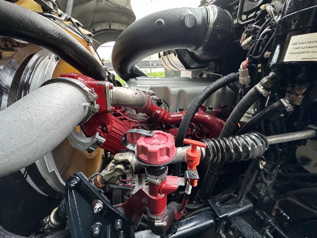 Engine compartment showing red fuel filter housing, red-painted components, large gray intake hose, and various black hoses in a Mack GU713 vacuum truck.