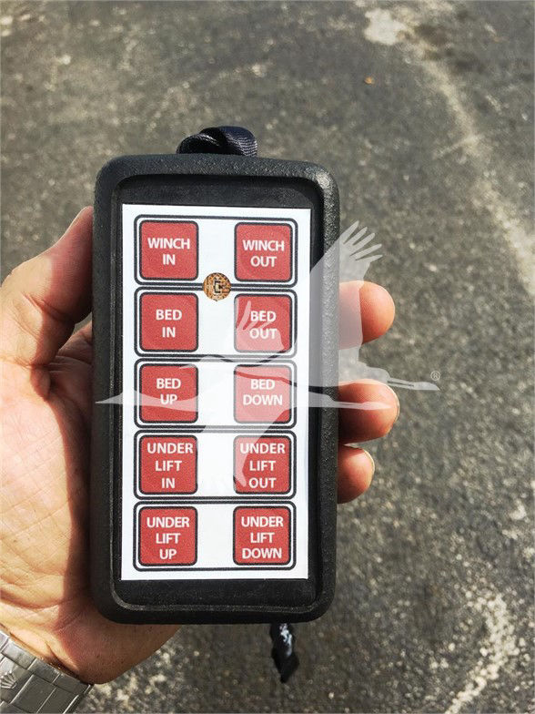 Remote control showing 12 labeled buttons: WINCH IN, WINCH OUT, BED IN, BED OUT, BED UP, BED DOWN, UNDER LIFT IN, UNDER LIFT OUT, UNDER LIFT UP, UNDER LIFT DOWN.  A small central circle shows a partial logo.