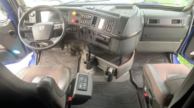 Volvo truck cab interior showing steering wheel, dashboard controls, and driver-seat area with center console; dual bench seating and rubber floor mats.