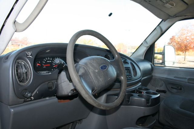 Ford E-Series van interior showing steering wheel, dashboard with gauge cluster, center console, and driver-side door.