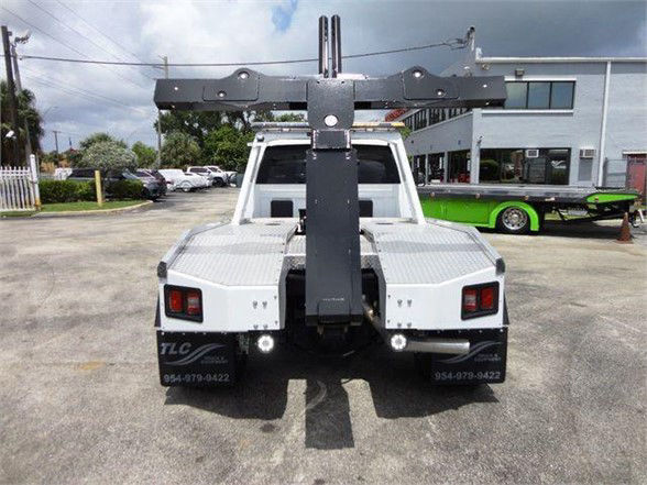 Truck rear view with large overhead crane boom, white bed, and dual taillights. Visible text includes contact numbers on rear bumper and the vehicle appears to be a 2024 Ram 4500 SLT tow truck.
