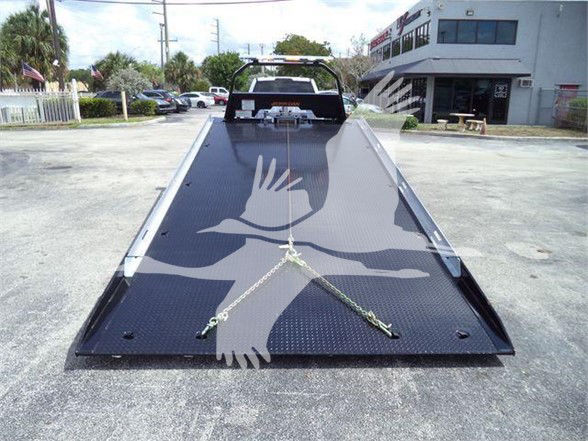 Flatbed tow truck bed with metal diamond plate, chains secured across the bed, and a cab in the distance.