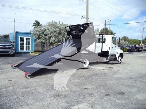 Hino 258LP hooklift truck with folded ramp in front of cab, white truck, black ramp, in a lot.