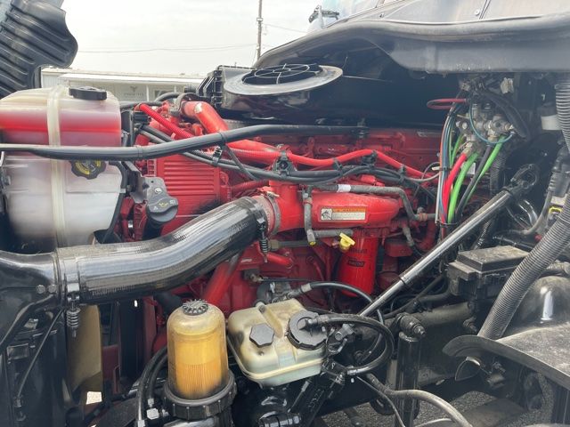 Engine bay of a 2013 Freightliner Cascadia showing red engine block, intake hose, coolant reservoir, and various hoses and wiring.