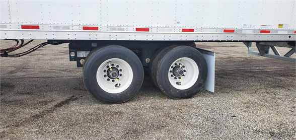 Trailer wheel tandem setup showing dual rear axles with white rims and black tires under a white dry van trailer.