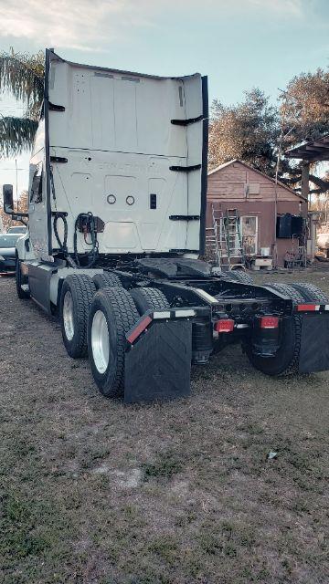 Truck tractor rear view showing fifth wheel and dual rear axles with white cab and open trailer area.
