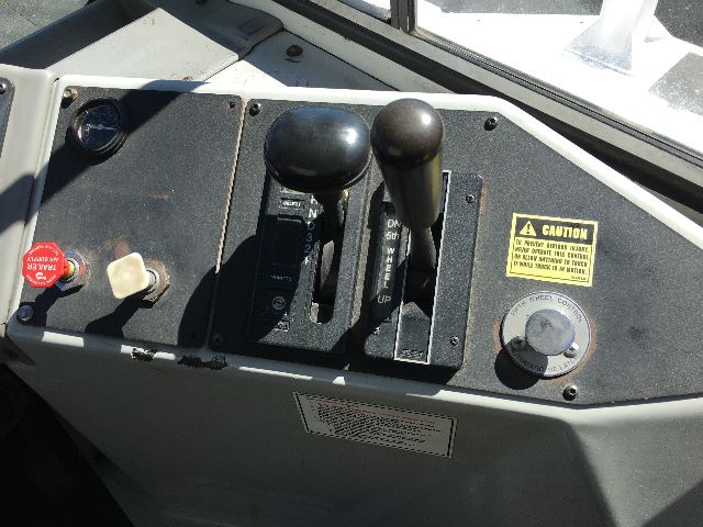 Operator cockpit with control levers and switches on Kalamar Ottawa YT30 yard crane cab; visible levers labeled forward/backward and parking, caution sticker, and red emergency stop button.