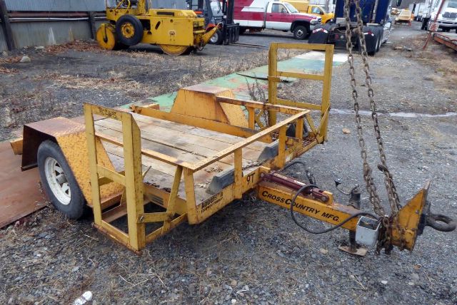 Cross Country trailer frame showing yellow-painted chassis, deck rails, wheeled axle, and hitch with chain; weathered surface.