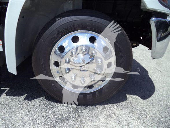 Wheel of a white 2025 Hino L6 truck with chrome rim and lug nuts visible; partial fender and undercarriage shown.