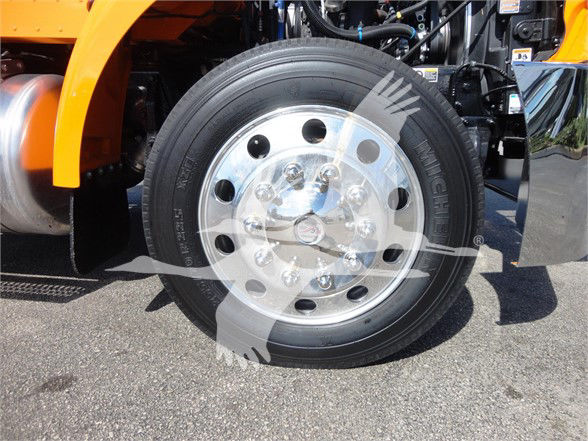 Truck wheel and front tire assembly showing polished steel hub with multiple lug holes and black tire on a Peterbilt 337. Partial orange bodywork visible.
