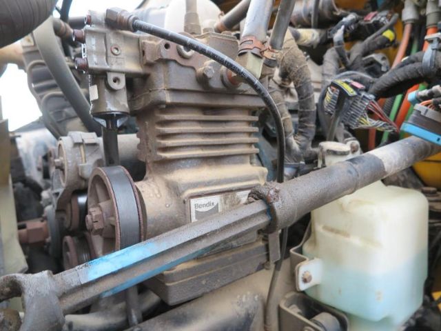 International diesel engine bay with visible compressor and belts, coolant reservoir, and wiring harnesses.