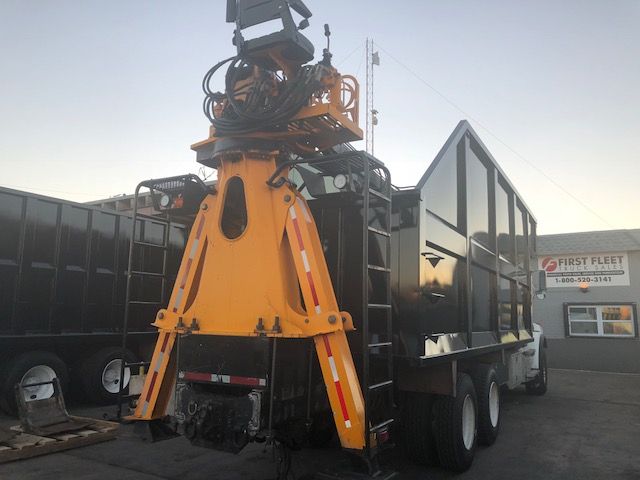 Truck with grapple attachment mounted on a Western Star dump body. Large yellow grapple arms with hydraulic hoses and metal frame, black dump bed, dual rear axles, in-yard.