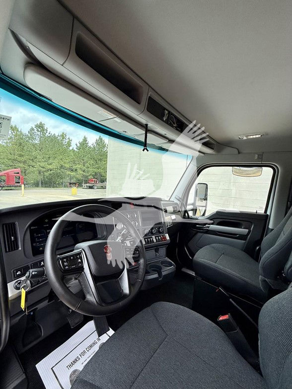 Kenworth T880 truck interior showing steering wheel, dashboard with multiple gauges, center console, driver seat, and passenger seat. Large windshield with sun visor area and overhead storage, front cab area.