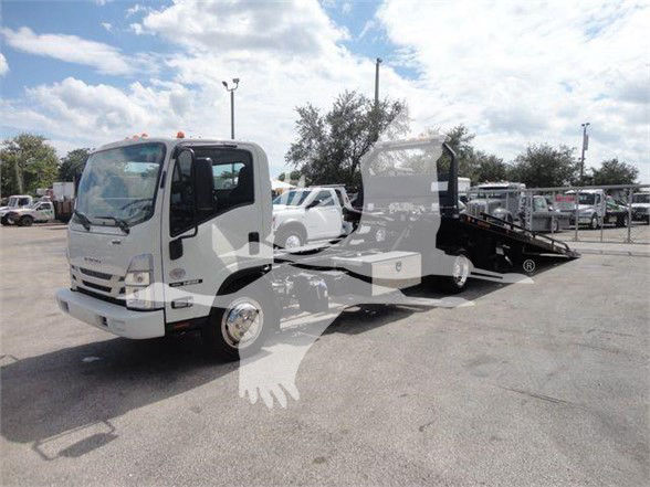 Isuzu NRR tow truck with a flatbed, white cab, black tow bed, and other trucks in background.