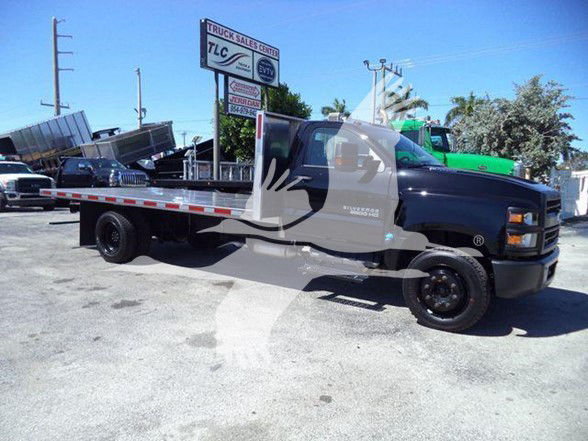 Flatbed dump truck showing Chevrolet Silverado 6500HD with black cab and aluminum flatbed.