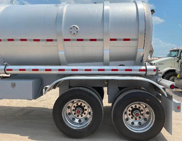 Aluminum DOT407 crude oil tanker trailer, 200BBL capacity, side view showing twin rear axles and tank with manhole access and reflective red/white stripes.