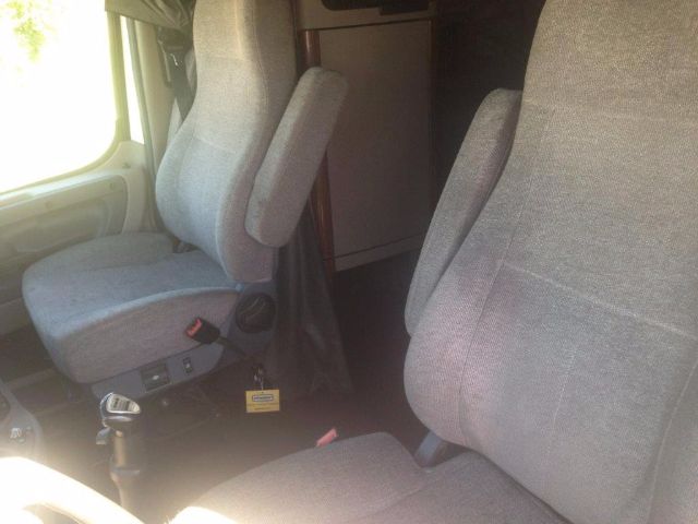 cab interior of a 2012 Freightliner Cascadia showing two gray fabric seats with armrests and a small control panel near the driver seat.
