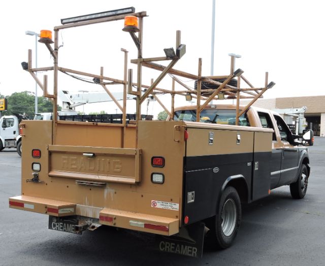 Ford F-350 utility pickup rear view with wooden ladder rack and tools in bed.