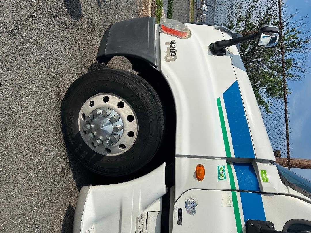 Truck cab side showing wheel and front fender of a 2011 Freightliner Cascadia with blue and green diagonal stripes and a 4200 decal.