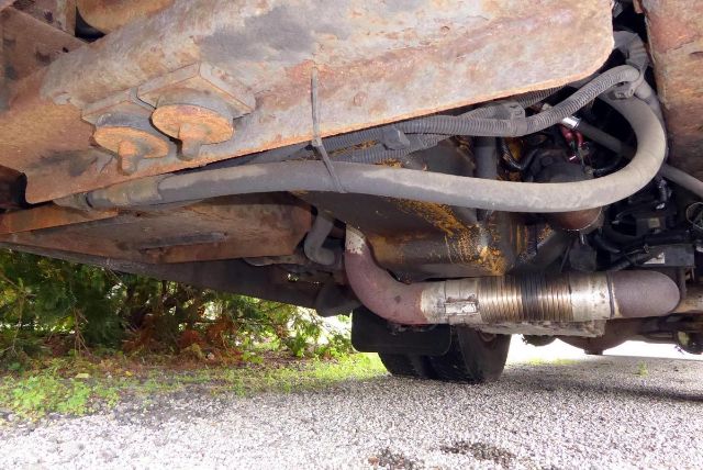 Underbelly of a bluebird All American bus showing exhaust pipe, suspension, and rusty shield.