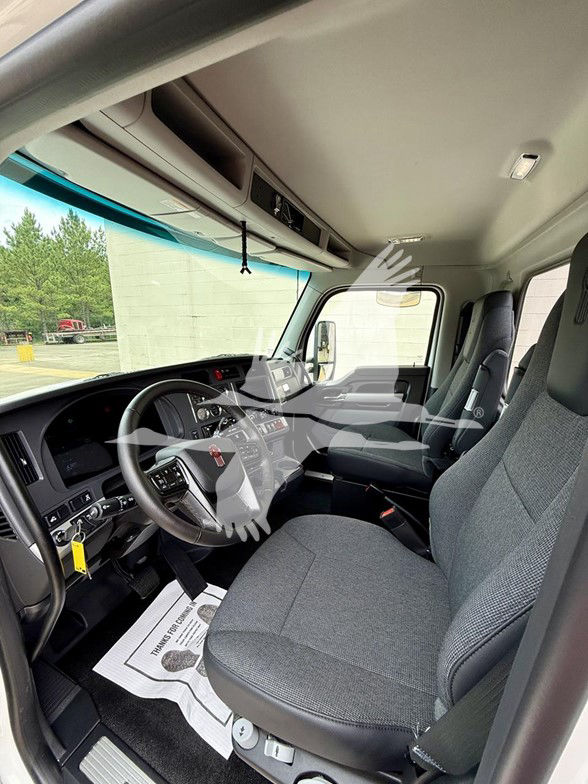 Kenworth T880 truck interior cab showing steering wheel, dashboard, and driver seat with grey fabric. Front windshield and passenger seat visible.