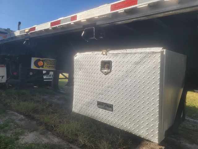 Flatbed trailer undercarriage showing a diamond plate aluminum tool chest mounted to the trailer frame.