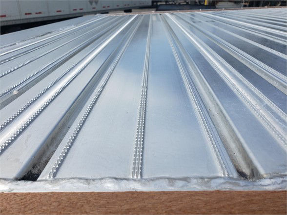 Flatbed trailer bed with aluminum sheets and corrugated ribs; close-up of the shiny metal surface.